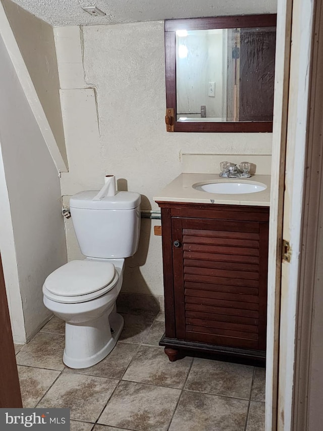 bathroom with toilet, tile flooring, vanity, and a textured ceiling