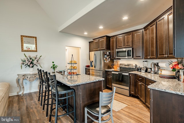 kitchen featuring light stone counters, appliances with stainless steel finishes, a center island, light hardwood / wood-style flooring, and a kitchen breakfast bar