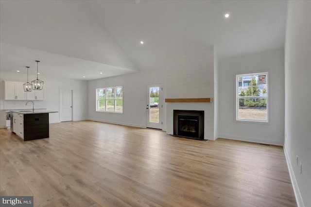 unfurnished living room featuring a fireplace, light hardwood / wood-style floors, sink, high vaulted ceiling, and a chandelier