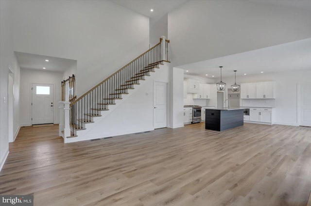 unfurnished living room featuring sink, light hardwood / wood-style floors, and a towering ceiling