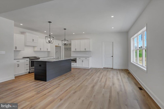 kitchen featuring white cabinets, decorative light fixtures, light wood-type flooring, and stainless steel range oven