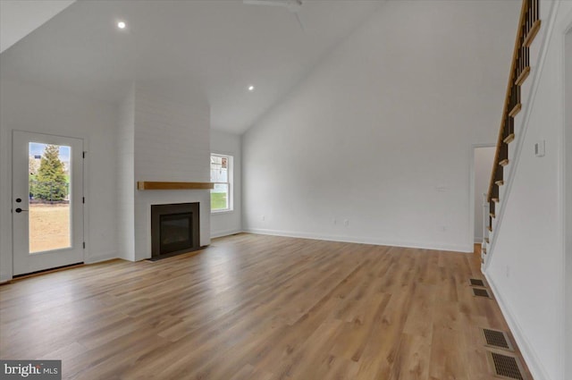 unfurnished living room with high vaulted ceiling, brick wall, light wood-type flooring, and a large fireplace