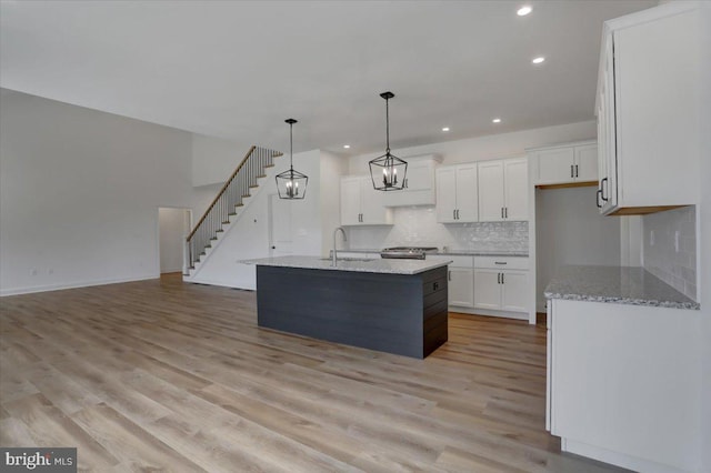 kitchen featuring white cabinetry, light wood-type flooring, a kitchen island with sink, pendant lighting, and sink