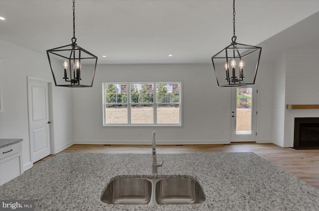 kitchen with light stone countertops, a wealth of natural light, sink, and light hardwood / wood-style flooring