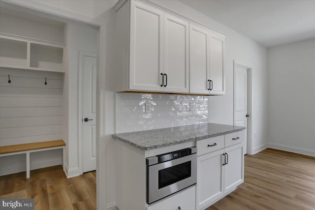 kitchen with light wood-type flooring, light stone counters, backsplash, white cabinetry, and oven