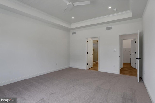 unfurnished bedroom with ceiling fan, light colored carpet, a tray ceiling, and ensuite bathroom