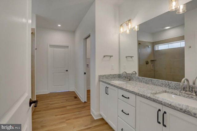 bathroom with double sink vanity, tiled shower, and hardwood / wood-style floors