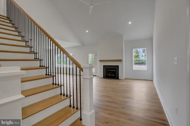 staircase with high vaulted ceiling, light hardwood / wood-style flooring, a large fireplace, and a healthy amount of sunlight