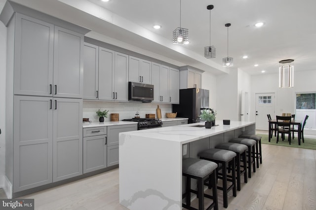 kitchen featuring appliances with stainless steel finishes, pendant lighting, an island with sink, light hardwood / wood-style floors, and light stone countertops