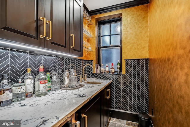 kitchen featuring dark brown cabinets, crown molding, tile flooring, light stone countertops, and backsplash