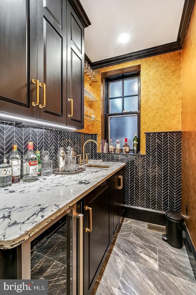 kitchen featuring tasteful backsplash, light stone counters, dark tile flooring, beverage cooler, and crown molding