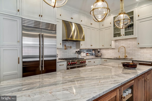 kitchen with light stone counters, backsplash, high quality appliances, wall chimney exhaust hood, and white cabinets