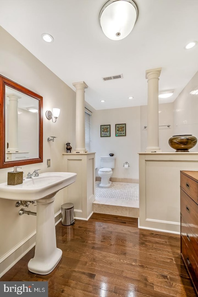 bathroom with toilet, decorative columns, and hardwood / wood-style flooring