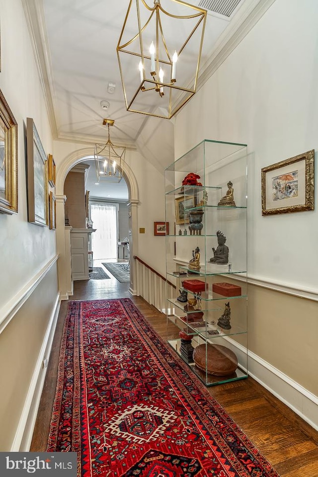 corridor with crown molding, dark wood-type flooring, and a chandelier