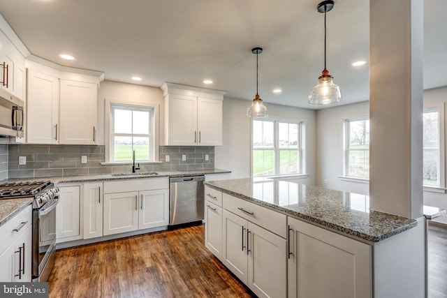 kitchen featuring appliances with stainless steel finishes, sink, backsplash, hanging light fixtures, and dark hardwood / wood-style floors