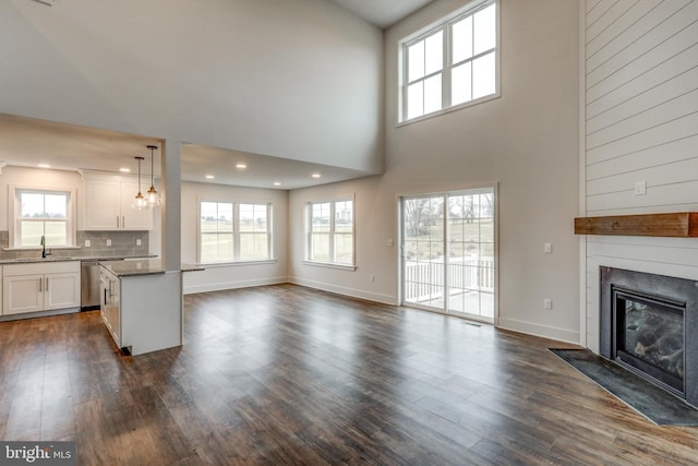 unfurnished living room with sink, a towering ceiling, and dark hardwood / wood-style floors