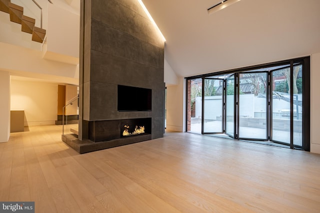 unfurnished living room featuring a large fireplace, a towering ceiling, and light hardwood / wood-style floors