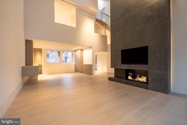 unfurnished living room with a fireplace, light hardwood / wood-style flooring, and a towering ceiling