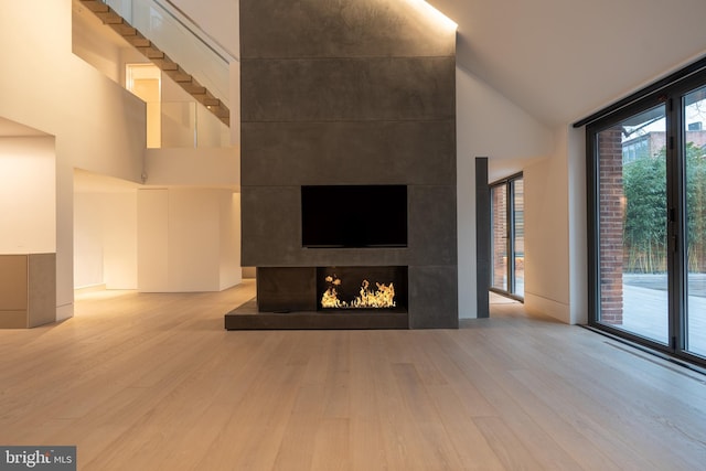 unfurnished living room featuring a towering ceiling, expansive windows, a tile fireplace, and light hardwood / wood-style floors