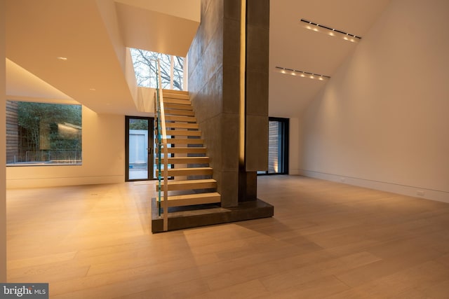 stairway with track lighting, high vaulted ceiling, and hardwood / wood-style floors