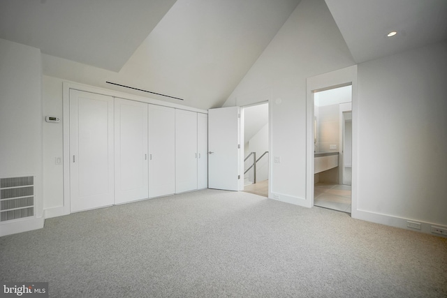 unfurnished bedroom featuring light colored carpet, connected bathroom, a closet, and lofted ceiling