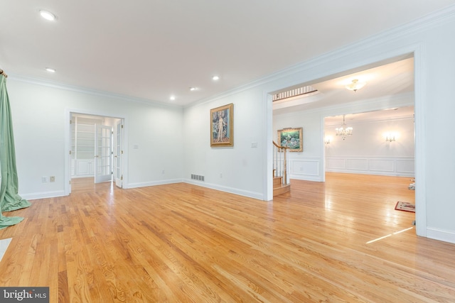 unfurnished living room featuring light wood-type flooring, crown molding, and an inviting chandelier