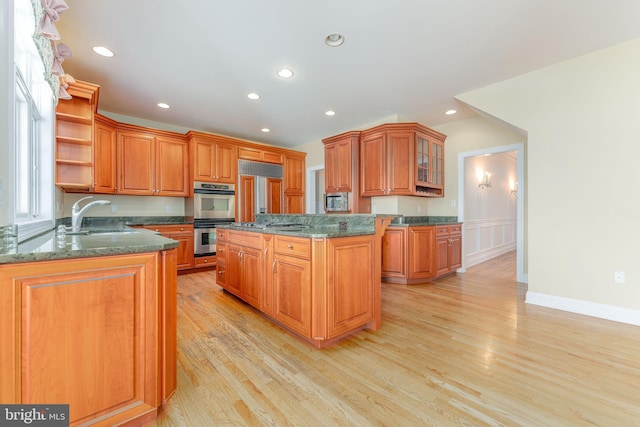 kitchen with a kitchen island, light wood-type flooring, stainless steel double oven, and dark stone countertops