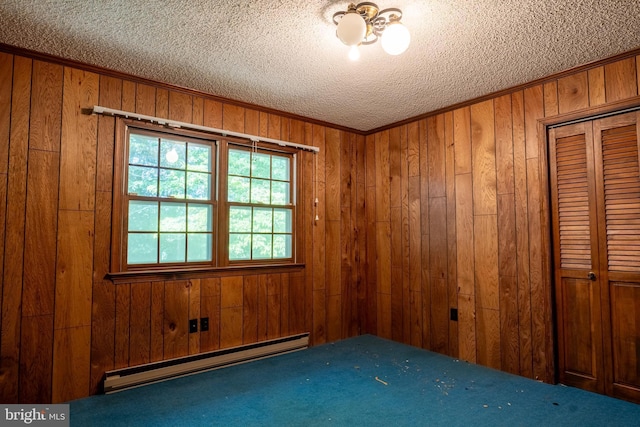 empty room with wood walls, a baseboard radiator, and a textured ceiling