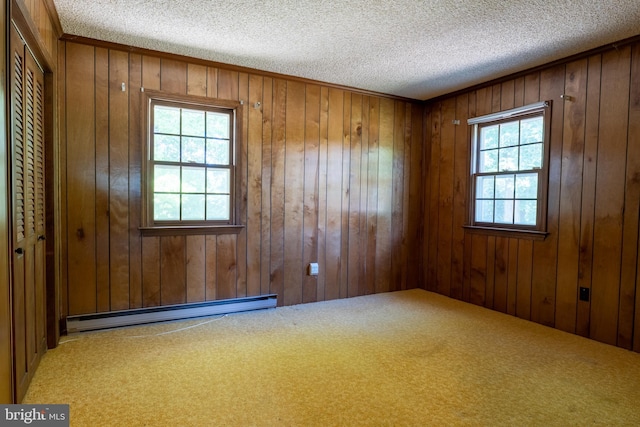 carpeted empty room featuring a textured ceiling, wooden walls, and a baseboard heating unit