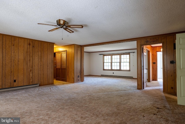 empty room featuring wood walls, light carpet, a baseboard heating unit, ceiling fan, and a textured ceiling