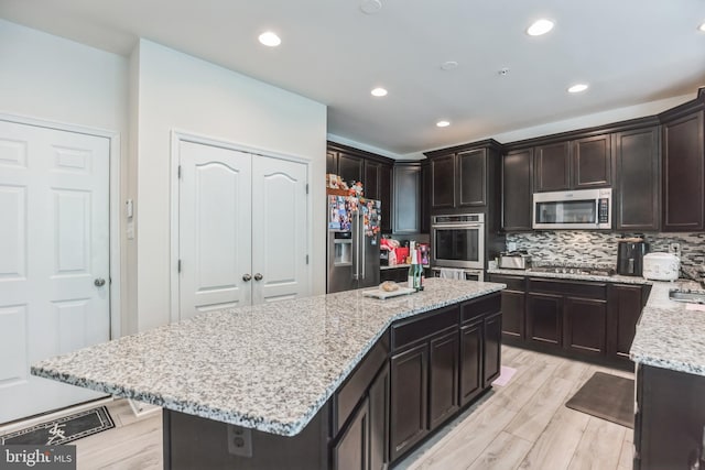 kitchen with light stone countertops, stainless steel appliances, tasteful backsplash, dark brown cabinetry, and a center island