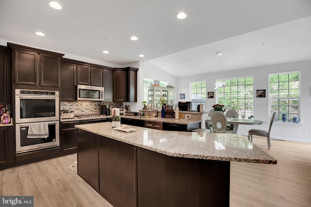 kitchen with a kitchen island, vaulted ceiling, stainless steel appliances, and light stone counters