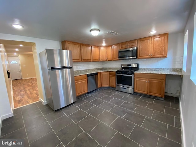 kitchen with backsplash, appliances with stainless steel finishes, sink, dark tile floors, and light stone counters