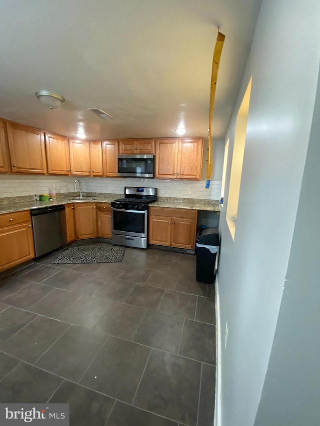 kitchen with appliances with stainless steel finishes, dark tile flooring, tasteful backsplash, and sink