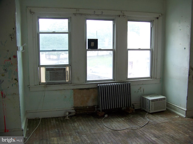 unfurnished room featuring radiator, hardwood / wood-style floors, and a healthy amount of sunlight