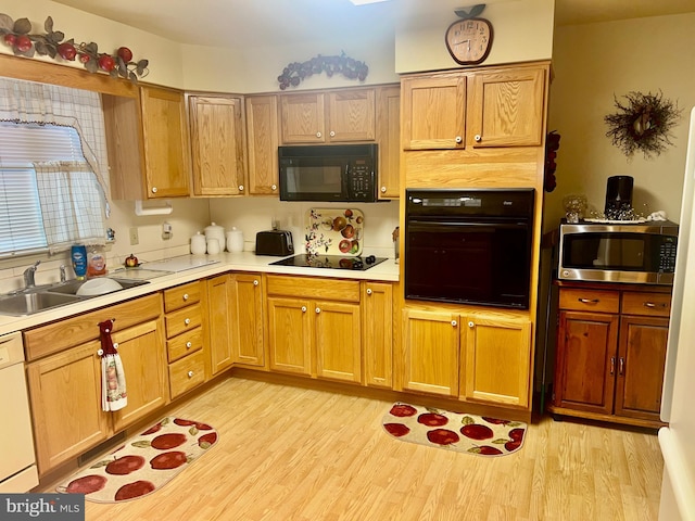 kitchen featuring a sink, black appliances, light countertops, and light wood-style floors