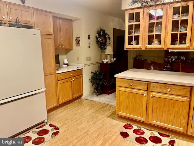 kitchen with glass insert cabinets, freestanding refrigerator, light countertops, and light wood-style floors