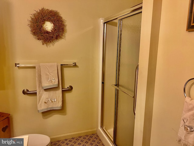 bathroom featuring toilet, a shower stall, and baseboards