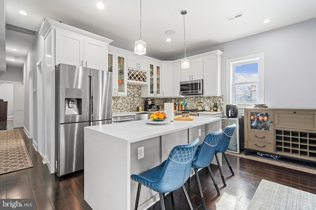 kitchen featuring appliances with stainless steel finishes, a kitchen island, backsplash, dark wood-type flooring, and white cabinetry