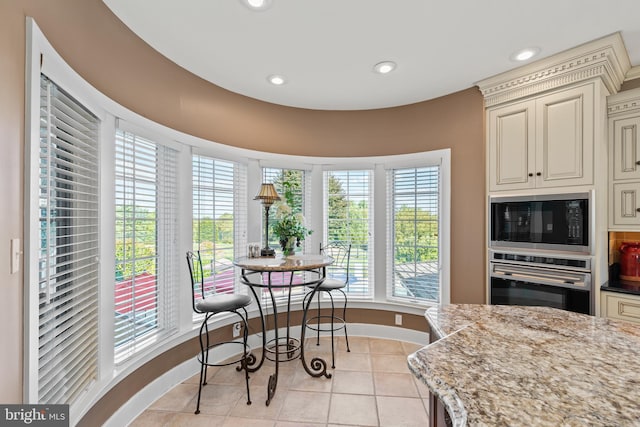 kitchen featuring light stone counters, light tile floors, oven, black microwave, and cream cabinetry