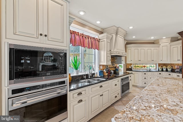 kitchen with custom exhaust hood, light tile flooring, black appliances, backsplash, and sink