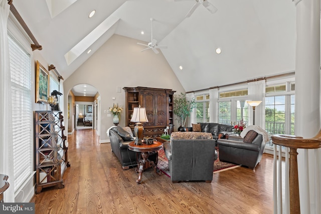 living room featuring a skylight, high vaulted ceiling, ceiling fan, and light wood-type flooring