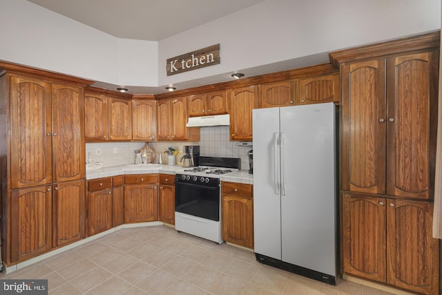 kitchen featuring tile countertops, light tile patterned flooring, white appliances, and tasteful backsplash