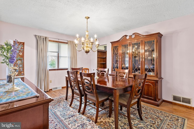 dining room featuring a textured ceiling, an inviting chandelier, and light wood-type flooring