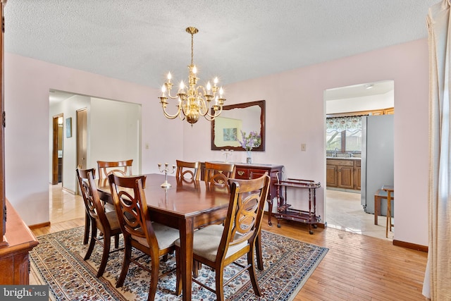 dining space with light hardwood / wood-style flooring, sink, a notable chandelier, and a textured ceiling