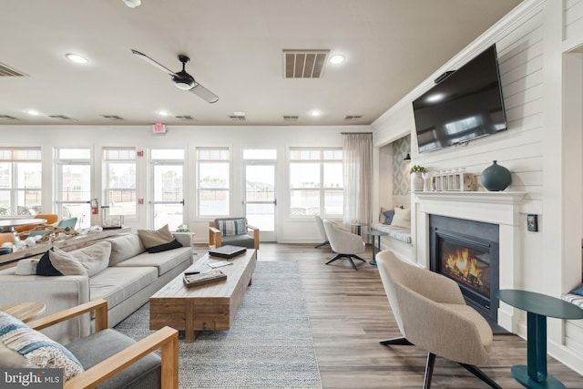 living area featuring ceiling fan, visible vents, wood finished floors, and a glass covered fireplace