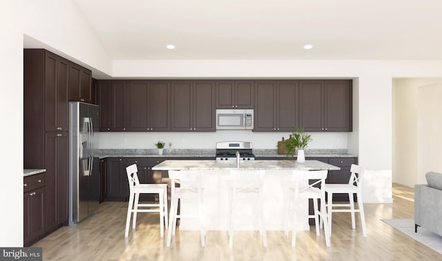 kitchen featuring a breakfast bar area, a kitchen island with sink, dark brown cabinetry, appliances with stainless steel finishes, and light wood-type flooring