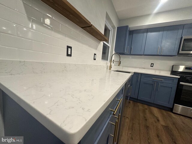 kitchen with blue cabinetry, sink, dark wood-type flooring, stainless steel appliances, and backsplash