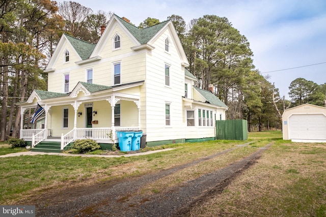 view of front of property featuring covered porch, a garage, a front yard, and an outdoor structure