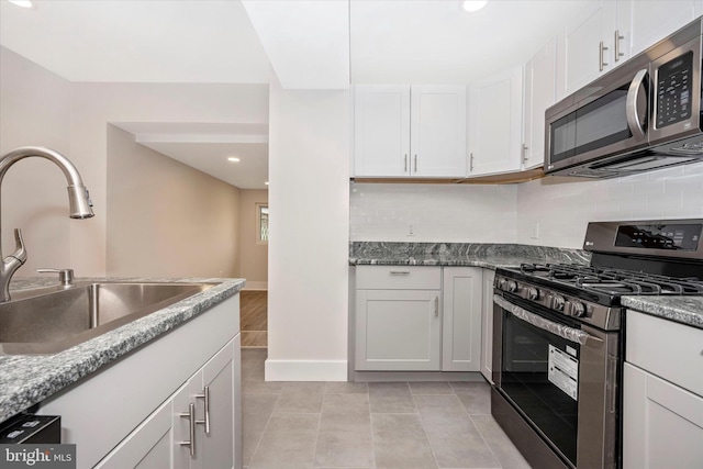 kitchen featuring appliances with stainless steel finishes, white cabinets, stone countertops, tasteful backsplash, and light tile flooring